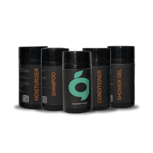 A collection of black September Forest hotel toiletries, including moisturizer, shampoo, conditioner, and shower gel.